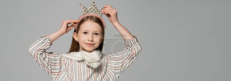 happy girl adjusting crown on head and smiling isolated on grey, banner 
