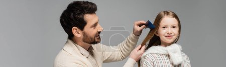 Foto de Happy bearded father brushing hair of smiling daughter isolated on grey, banner - Imagen libre de derechos