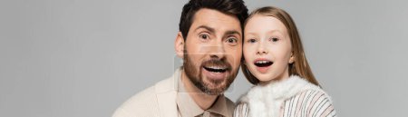 portrait of amazed father and daughter looking at camera isolated on grey, banner 