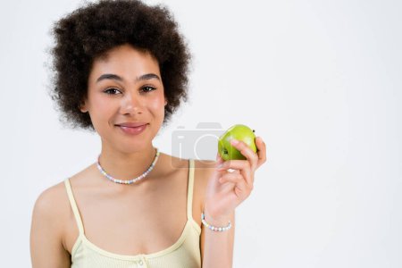 Retrato de una mujer afroamericana sonriente sosteniendo manzana fresca aislada en gris 