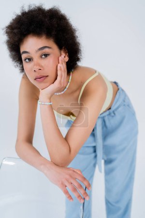 Porträt einer jungen Afroamerikanerin posiert in der Nähe von Stuhl isoliert auf grau 