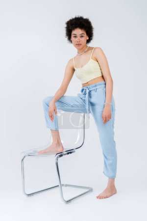 Full length of african american model posing near chair on grey background 