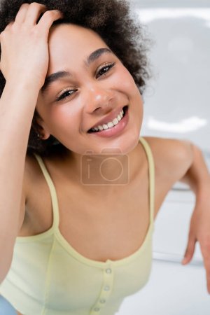 Portrait of positive african american woman sitting near blurred chair on grey background 