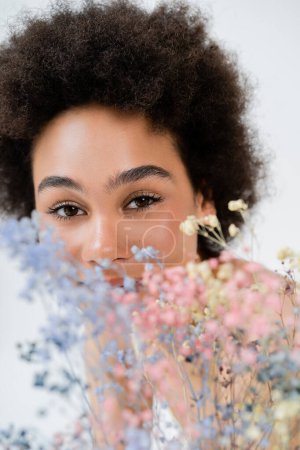 Photo for African american woman looking at camera near blurred flowers isolated on grey - Royalty Free Image