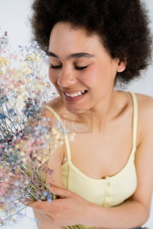 Happy african american woman holding baby breath flowers isolated on grey 
