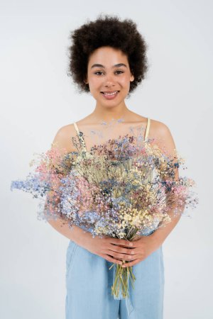 Cheerful african american woman holding flowers isolated on grey 