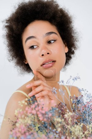 Portrait of african american woman touching face near baby breath flowers isolated on grey 