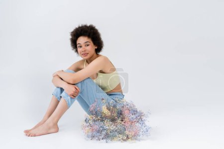 Barefoot african american woman sitting near baby breath flowers on grey background 