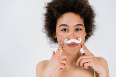 African american woman with paper moustache looking at camera isolated on grey 