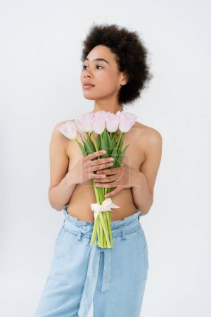 Mujer afroamericana con pecho desnudo sosteniendo flores de tulipán aisladas en gris 