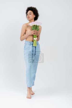 Foto de Mujer afroamericana descalza con el pecho desnudo sosteniendo tulipanes sobre fondo gris - Imagen libre de derechos