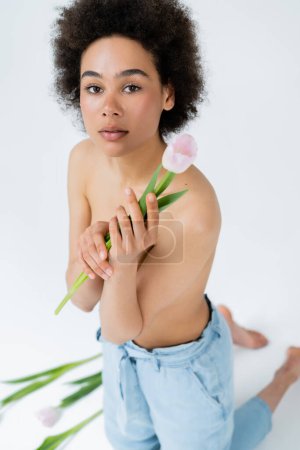 Mujer afroamericana con hombros desnudos sosteniendo tulipán rosa sobre fondo gris 