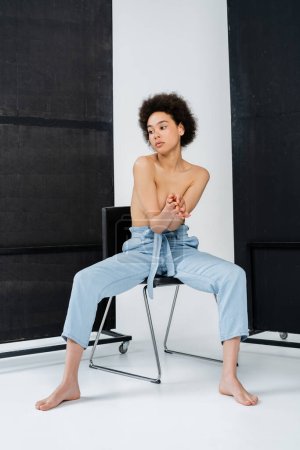 Shirtless african american woman posing on chair on grey and black background 