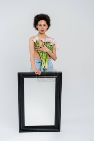 Hemdlose afrikanisch-amerikanische Frau mit Tulpen und Spiegel auf grauem Hintergrund 