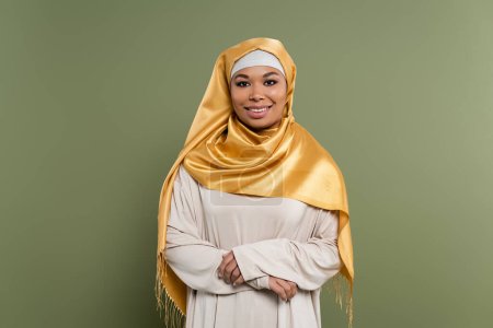 Smiling multiracial woman in hijab looking at camera on green background