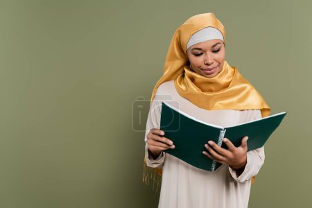 Multirassische muslimische Studentin blickt auf Notizbuch auf grünem Hintergrund
