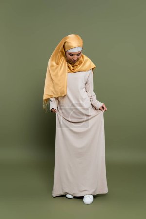 Stilvolle multirassische Frau im Hijab steht im Kleid auf grünem Hintergrund