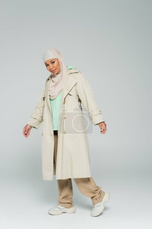 volle Länge der multirassischen muslimischen Frau in trendigem lässigem Outfit und Hijab, die in die Kamera auf grauem Hintergrund blickt