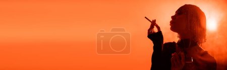 Téléchargez les photos : Silhouette ombragée de femme sexy glamour avec cigarette sur fond orange avec rétro-éclairé et fumée, bannière - en image libre de droit