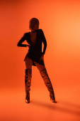 full length of woman in long silver boots and sexy dress posing with hand on hip on orange background Poster #645513484