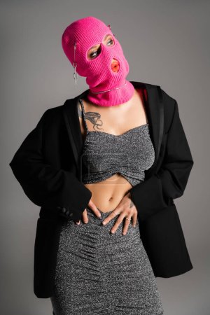 Photo for Sexy tattooed woman posing in fashionable clothes and pink balaclava isolated on grey - Royalty Free Image