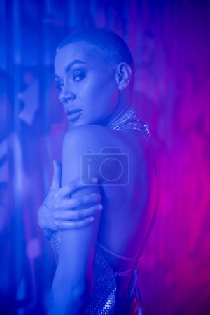 mujer tatuada apasionada mirando a la cámara en la iluminación azul y púrpura con humo
