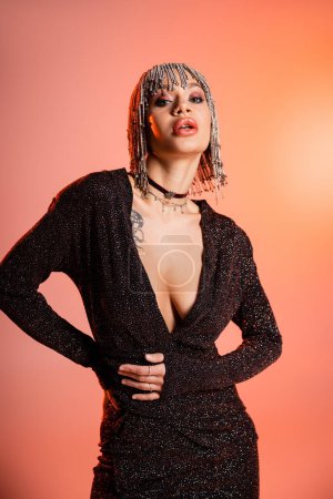 Téléchargez les photos : Femme séduisante avec corps sexy posant en perruque bijoux et robe lurex noir sur fond rose corail - en image libre de droit