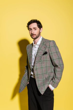 Stylish man in plaid jacket posing on yellow background with shadow