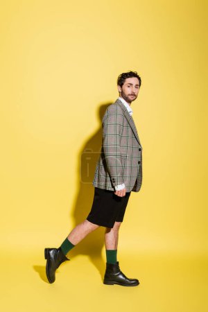 Full length of trendy model in shorts and jacket standing on yellow background 