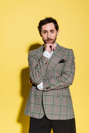 Téléchargez les photos : Portrait d'homme à la mode en veste à carreaux regardant la caméra sur fond jaune - en image libre de droit