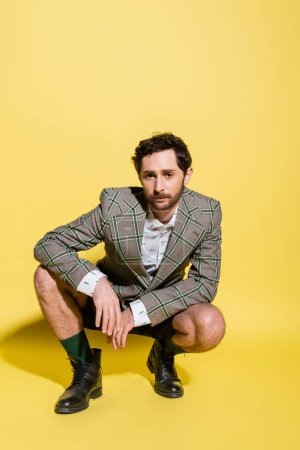 Trendy man in shorts and jacket posing on yellow background with shadow 