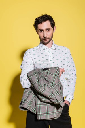 Photo for Brunette man in shirt holding checkered jacket on yellow background with shadow - Royalty Free Image