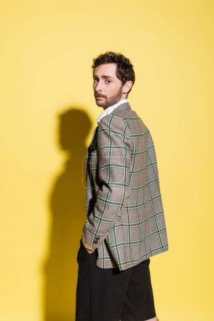 Trendy man in checkered jacket looking at camera on yellow background 