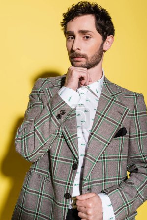 Portrait of trendy man in checkered jacket looking at camera on yellow background 