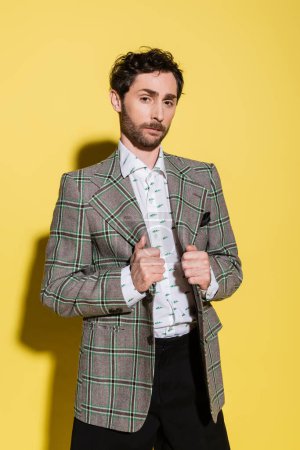 Photo for Bearded model adjusting jacket and looking at camera on yellow background - Royalty Free Image