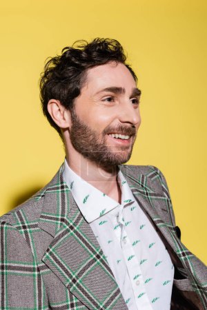 Portrait of smiling bearded man in shirt and jacket looking away on yellow background 