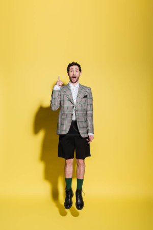 Excited stylish man pointing with finger and jumping on yellow background 