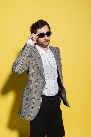 Photo for Trendy charming guy in jacket holding sunglasses on yellow background - Royalty Free Image