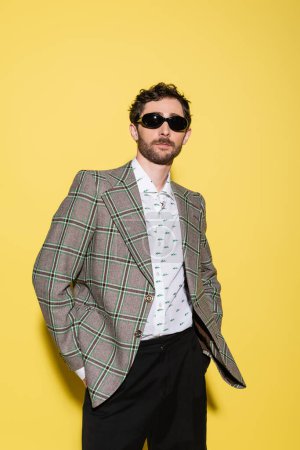 Photo for Trendy model in sunglasses and plaid jacket standing on yellow background - Royalty Free Image