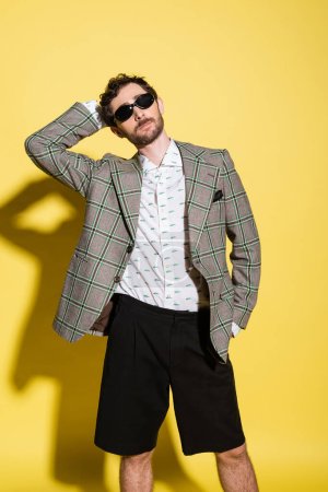 Fashionable model posing in sunglasses and jacket on yellow background 