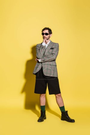 Photo for Charming guy in sunglasses and jacket posing on yellow background - Royalty Free Image