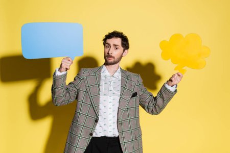 Photo for Stylish man holding speech and thought bubbles on yellow background - Royalty Free Image