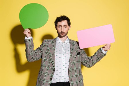 Photo for Charming guy in jacket holding speech bubbles on yellow background - Royalty Free Image
