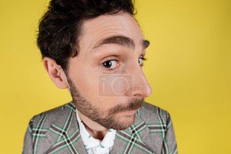 Amplia vista angular del hombre barbudo con chaqueta mirando a la cámara aislada en amarillo  
