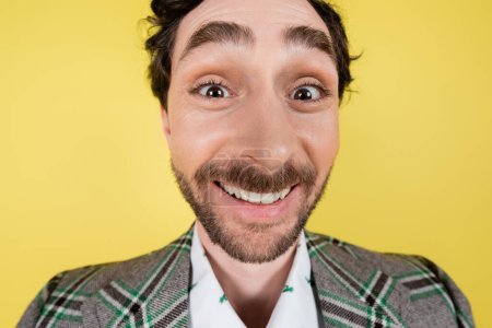 Weitwinkelbild eines fröhlichen Mannes in karierter Jacke, der isoliert auf gelb in die Kamera blickt  