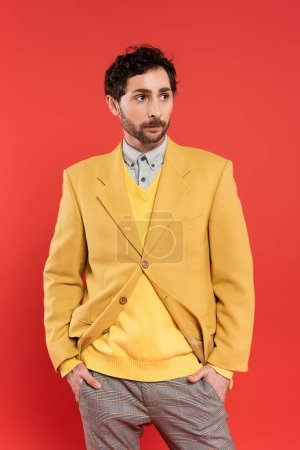 Foto de Charming chico en chaqueta amarilla cogido de la mano en bolsillos aislados en rojo - Imagen libre de derechos