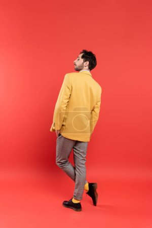 Foto de Vista lateral del hombre con estilo en chaqueta amarilla posando sobre fondo rojo coral - Imagen libre de derechos