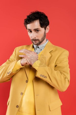 Retrato de tipo encantador en chaqueta amarilla apretando puño aislado en rojo 