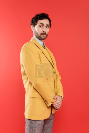 Téléchargez les photos : Élégant charmant gars en veste jaune debout sur fond rouge corail - en image libre de droit