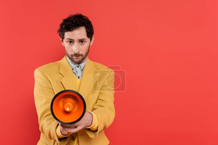 Trendy model in yellow jacket holding loudspeaker isolated on coral red 